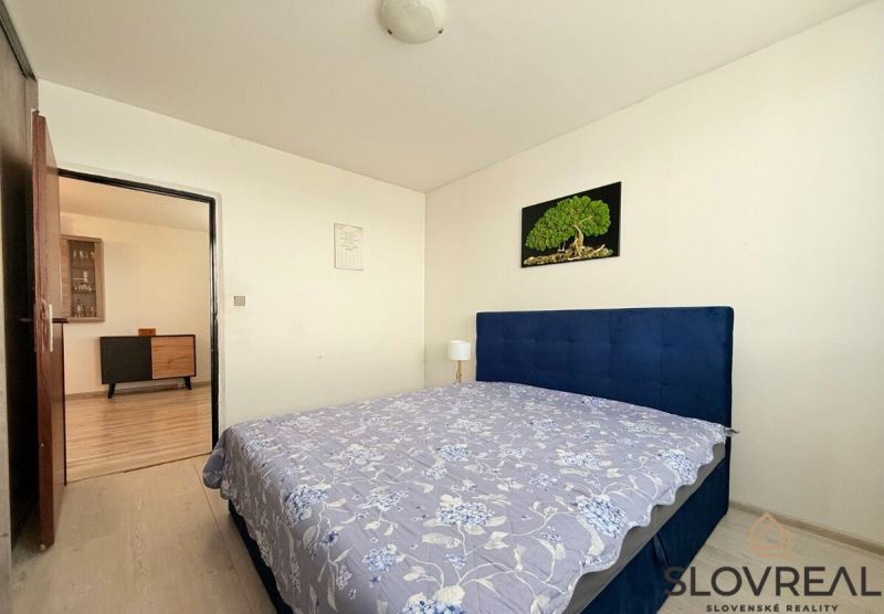 Schlafzimmer mit grauem Boden in einer 3-Zimmer-Wohnung, einfache Möbel und ein Bild an der Wand.
