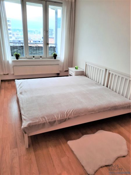 Helles Schlafzimmer in einer Zweizimmerwohnung mit Fenster und Boden in Holzoptik.