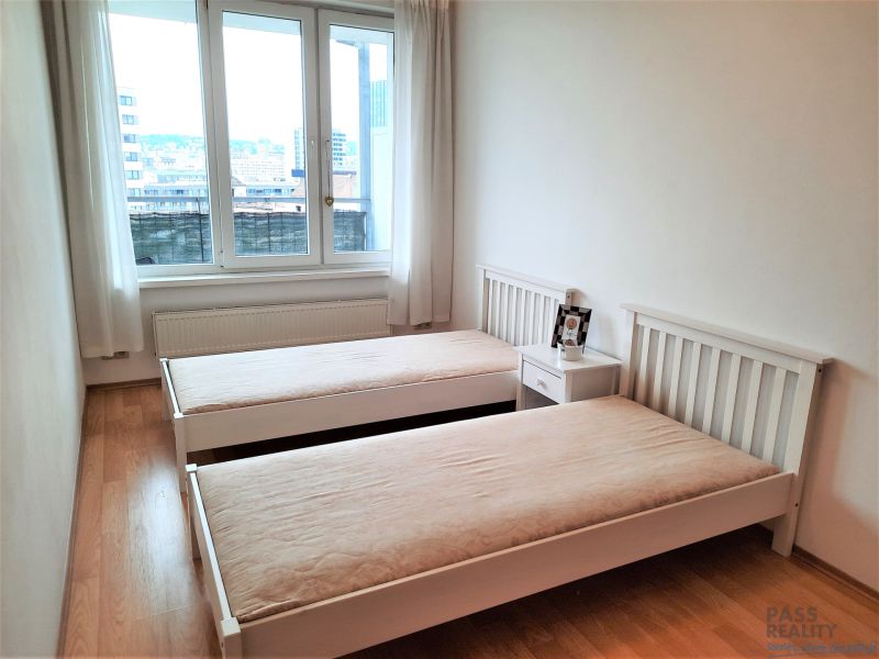 Schlafzimmer mit zwei Betten, einem Nachttisch und einem Boden mit Holzdekor in einer Zweizimmerwohnung.