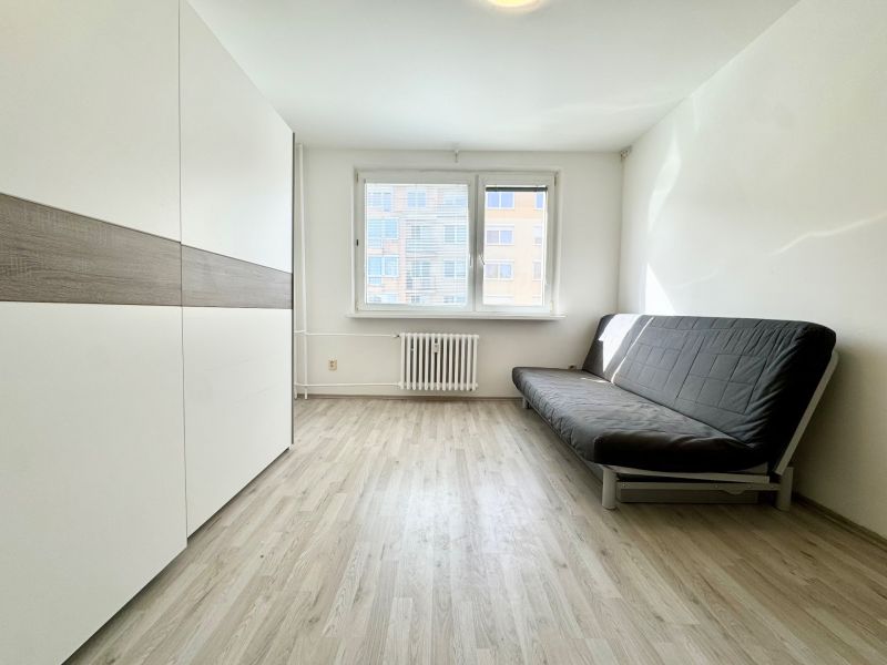 Ein Zimmer in einer 3-Zimmer-Wohnung mit Holzboden, schwarzem Sofa, Kleiderschrank.