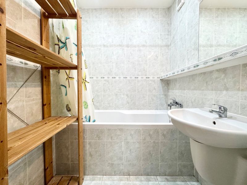 Badezimmer mit Duschvorhang, Holzregal und Waschbecken in einer 3-Zimmer-Wohnung.