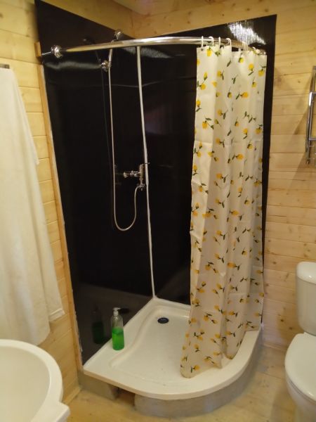 Duschkabine in der Hütte mit einem Blumenvorhang und einem Boden in Holzoptik.