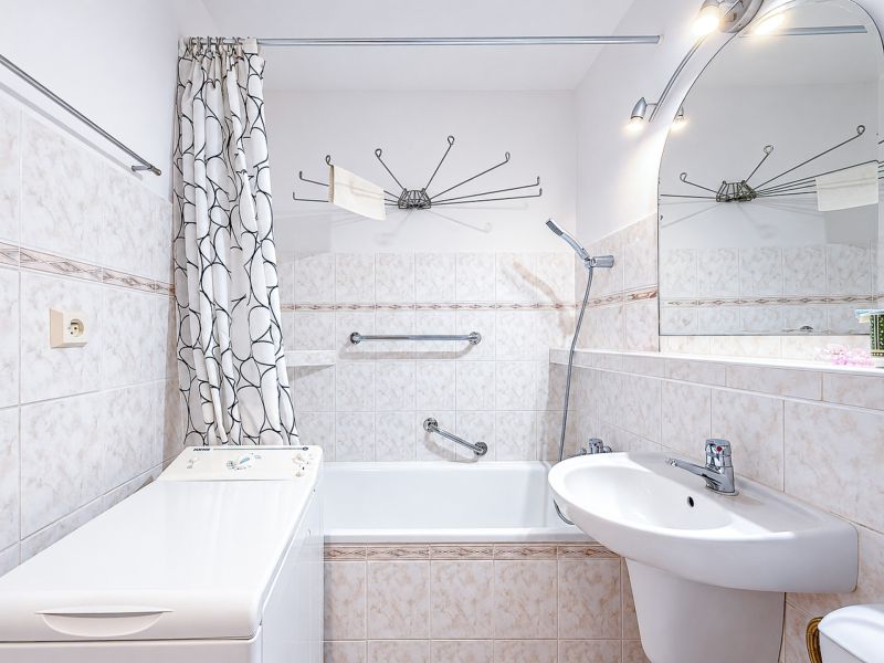 Badezimmer mit Vorhang, Badewanne, Waschbecken und Waschmaschine in einer Einzimmerwohnung.