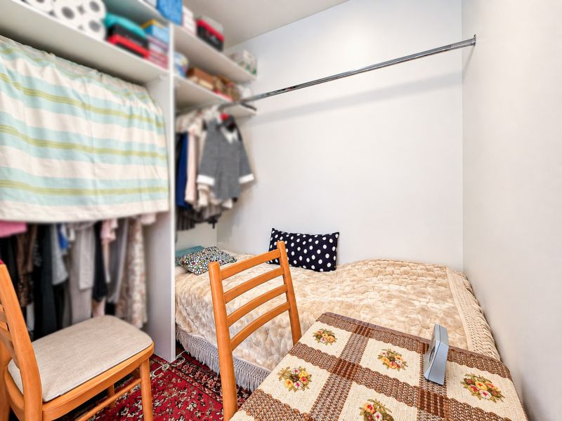 Ein Schlafzimmer mit Bett, Schrank und Stühlen in einer Einzimmerwohnung mit gemustertem Teppich.