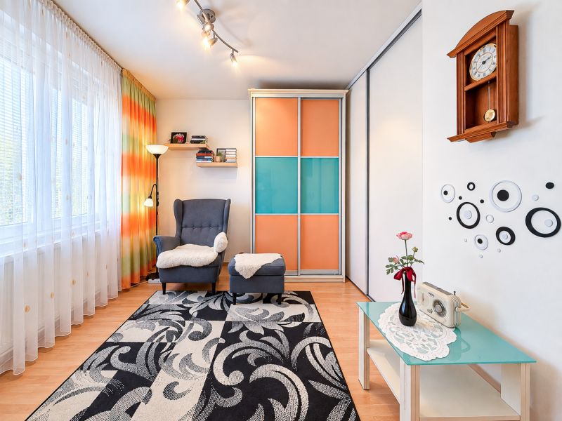 Wohnzimmer in einer Einzimmerwohnung mit einem bequemen Sessel, Teppich mit abstraktem Muster.