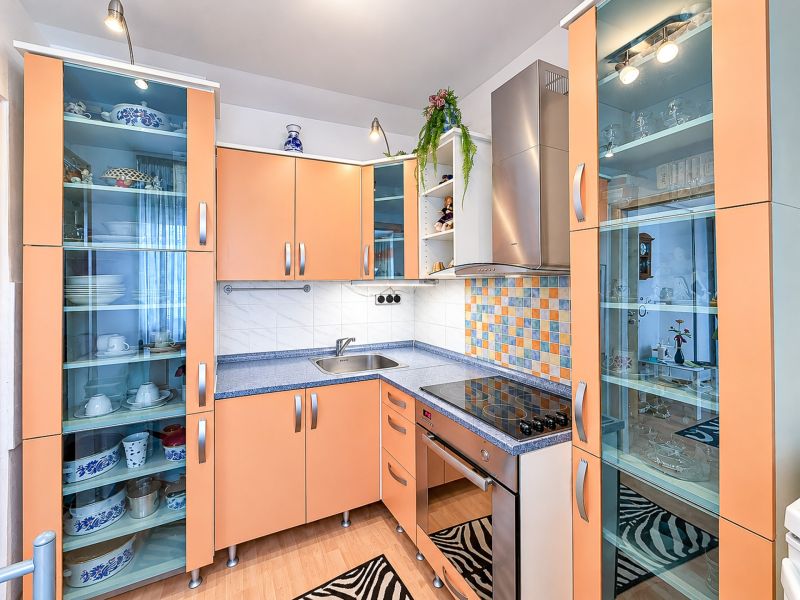 Küche in einer Einzimmerwohnung mit orangefarbenen Schränken, Glasvitrinen und Geräten.