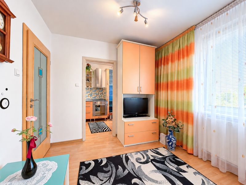 Eine Einzimmerwohnung mit hellen Wänden, orangefarbenen Möbeln und dekorativen Vorhängen.