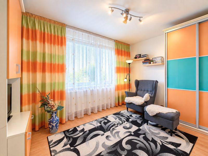 Wohnzimmer in einer Einzimmerwohnung mit bunten Vorhängen und einem Sessel auf einem Boden mit Holzdekor.