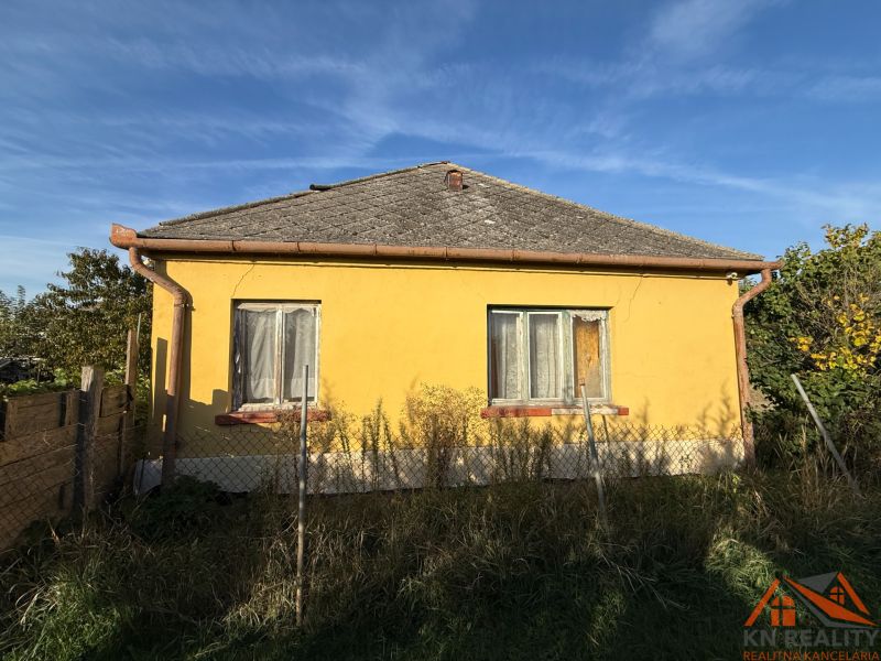 Gelbes Einfamilienhaus in Komárno mit Zaun und Garten unter blauem Himmel.