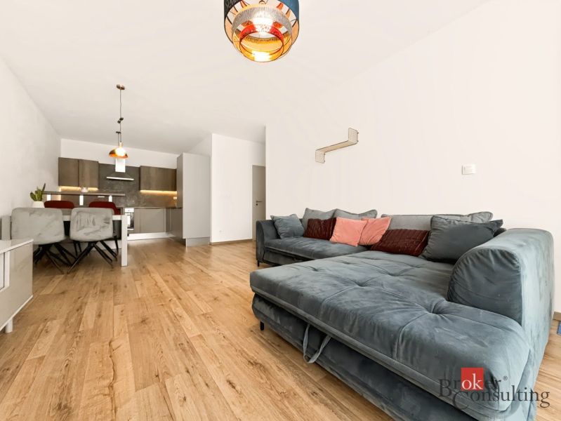 2-Zimmer-Wohnung mit bequemer Couch, Küche im Hintergrund, Boden mit Holzdekor.