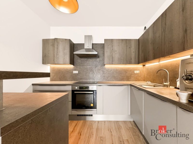 Küche in einer 2-Zimmer-Wohnung mit Holzboden und beleuchteten Schränken.