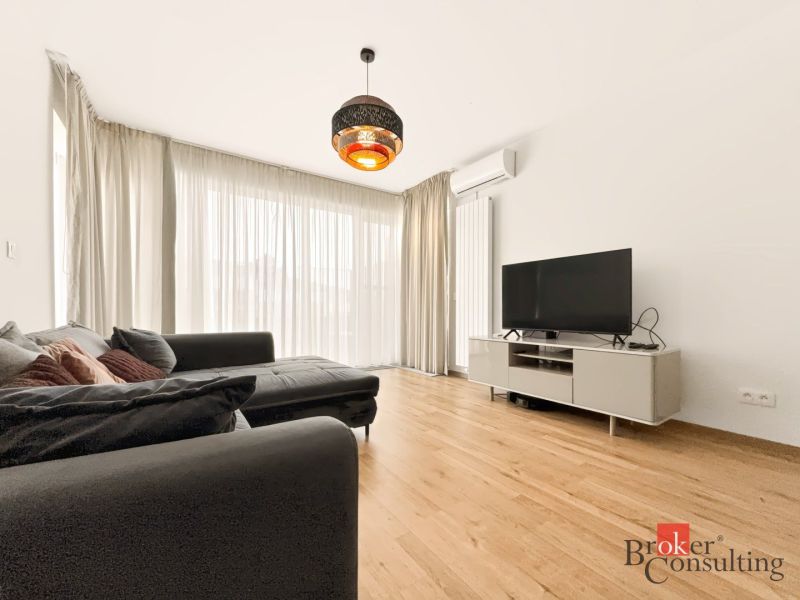 Wohnzimmer mit Holzboden, großem Sofa und Fernseher in einer 2-Zimmer-Wohnung.
