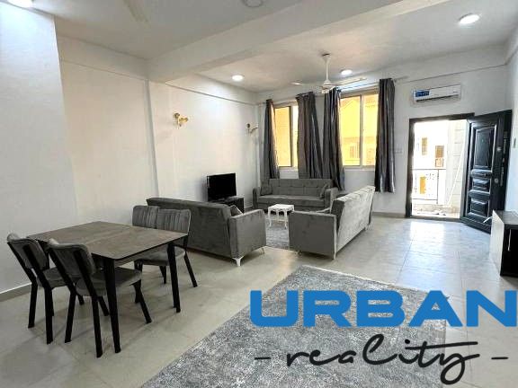 2-Zimmer-Wohnung mit dunklen Sofas, Esstisch und Fernseher, Boden mit Holzdekor.