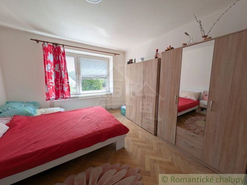 Schlafzimmer mit roter Bettwäsche, einem Schrank und einem Boden mit Holzdekor in einer 2-Zimmer-Wohnung.