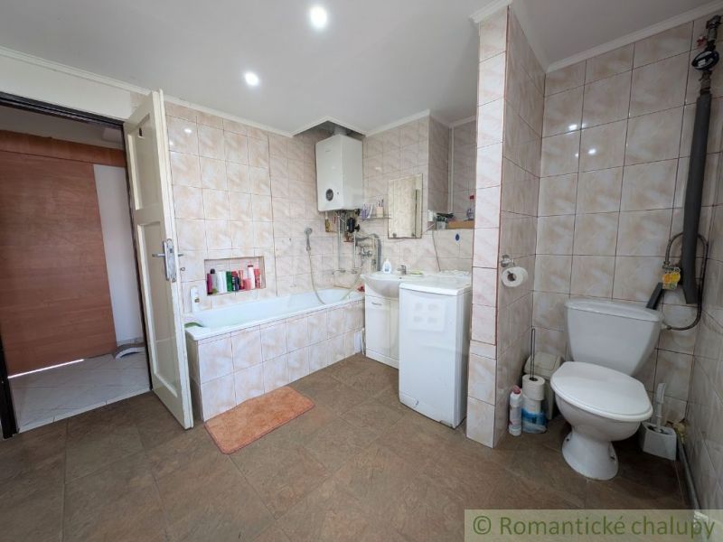 Badezimmer in einer 2-Zimmer-Wohnung mit Badewanne und Waschmaschine, gefliest mit hellen Fliesen.
