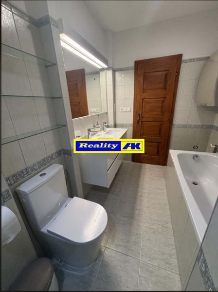 Ein Badezimmer mit Badewanne und Toilette in einem Einfamilienhaus, weiße Fliesen und Holztüren.