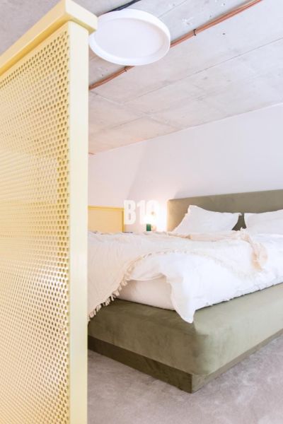Schlafzimmer in einer 2-Zimmer-Wohnung mit Bett und gelber Trennwand.