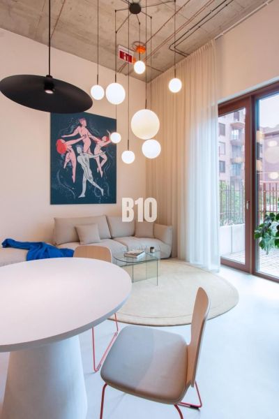 Wohnbereich mit weißen Möbeln, rundem Tisch und Kunst in einer 2-Zimmer-Wohnung.
