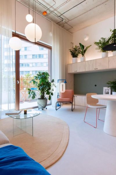 Helle Innenausstattung einer 2-Zimmer-Wohnung mit runden Leuchten, Pflanzen und einem Glastisch.