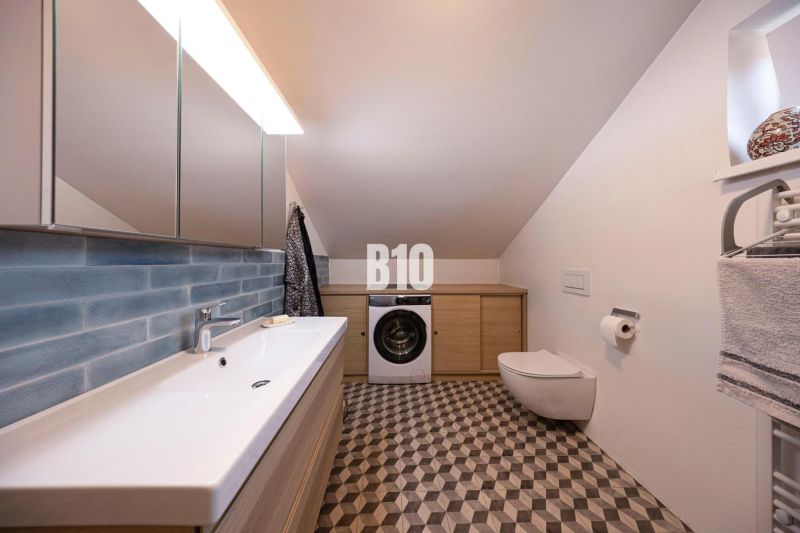 Badezimmer im Einfamilienhaus mit Waschmaschine, Spiegel und Waschbecken, geometrische Fliesen.