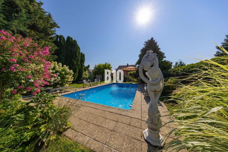 Ein Pool im Garten eines Einfamilienhauses in der Bratislavská-Straße in Malinovo mit Blumen und einer Statue.