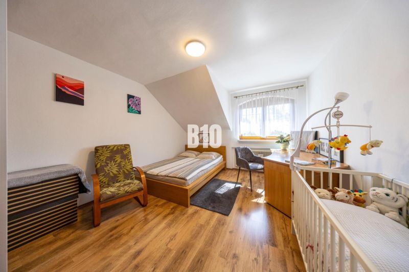 Schlafzimmer im Einfamilienhaus mit Bett, Kinderbett und Boden in Holzoptik.