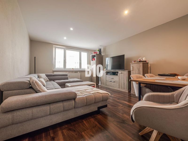 Wohnzimmer in einer 3-Zimmer-Wohnung mit einem bequemen Sofa und einem Boden in Holzoptik.