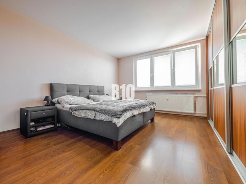 Schlafzimmer mit großem Bett, Nachttisch und Boden mit Holzdekor in einer 3-Zimmer-Wohnung.