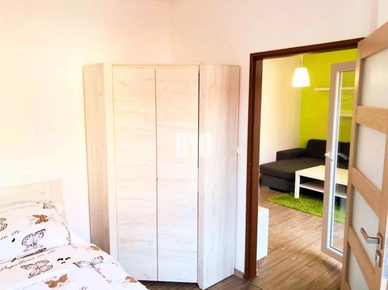 Schlafzimmer mit Eckschrank, nebenan der Eingang zum Wohnzimmer mit Sofa.