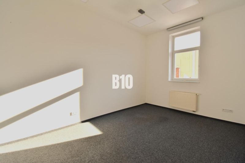 Büroinnenraum mit Teppichboden und Fenster, Blick auf eine Wand und Heizkörper.