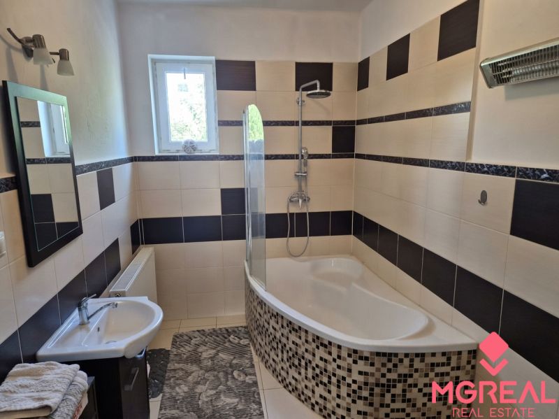 Badezimmer im Einfamilienhaus mit Badewanne, Fliesen und Fenster; dezente Ausstattung und Leuchte.