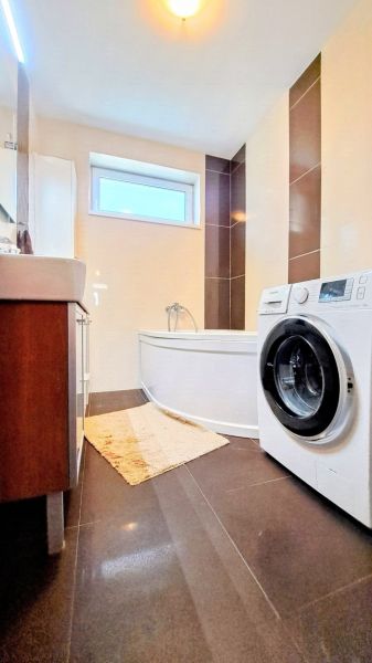 Badezimmer im Einfamilienhaus mit Badewanne, Waschmaschine und dunklen Fliesen im dekorativen Design.
