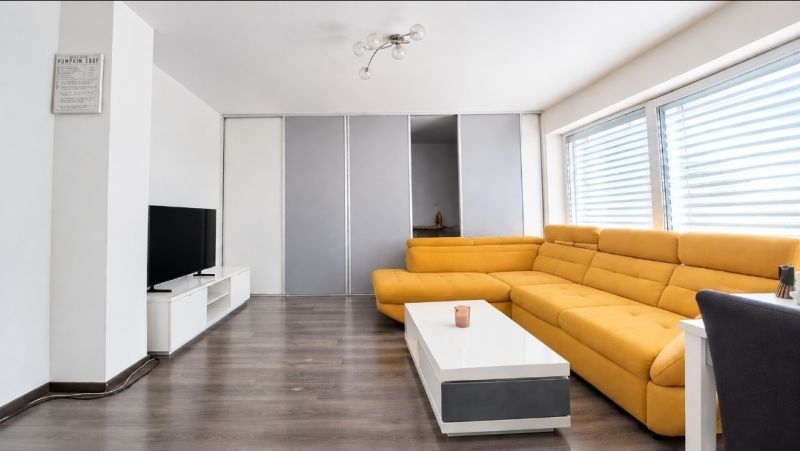 Wohnzimmer in einem Einfamilienhaus mit gelbem Sofa, Fernseher und Holzboden.