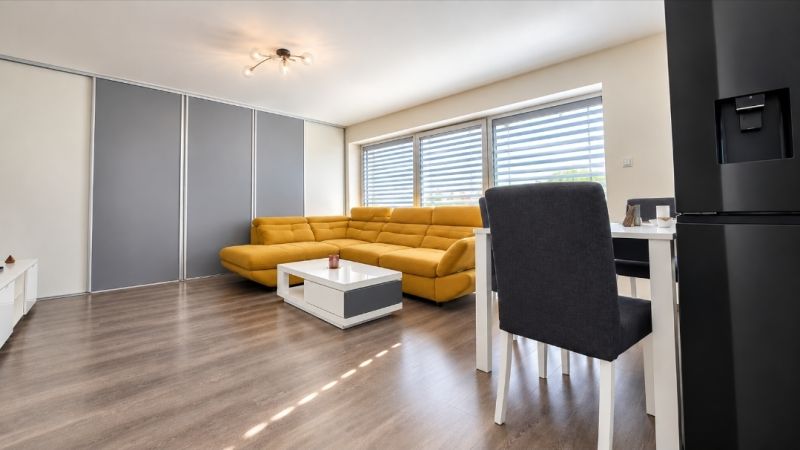 Wohnzimmer mit Holzdekorboden, gelbem Sofa und Esstisch.