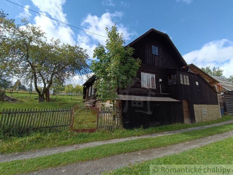 Eine Holzhütte in Staškov, umgeben von Bäumen und einem Zaun auf einer geräumigen grünen Fläche.