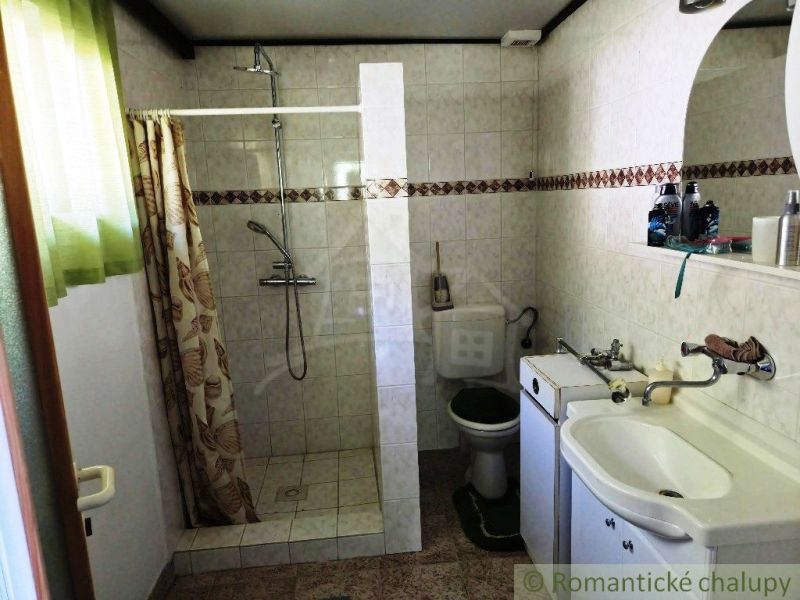 Badezimmer in der Hütte mit weißen Fliesen, Dusche und Waschbecken mit Spiegel.
