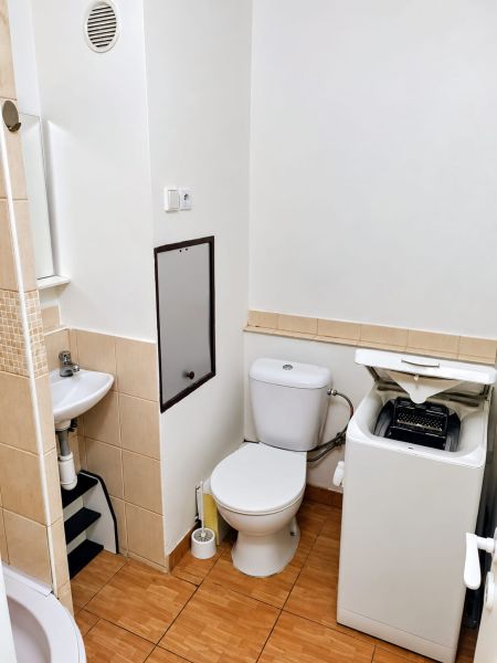 Badezimmer in einem Studio-Apartment mit Waschmaschine, Toilette und Waschbecken, Boden mit Holzdekor.