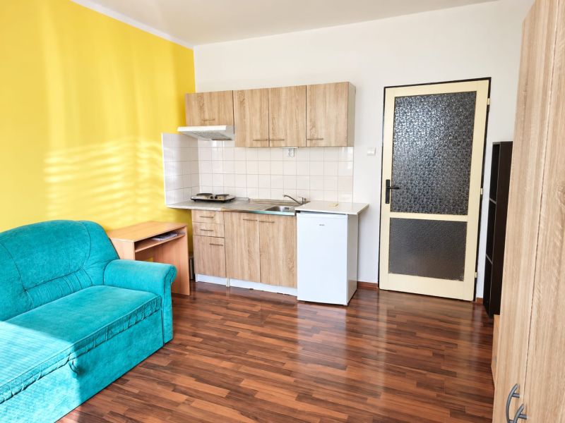 Einzimmerwohnung mit gelber Wand, Küchenzeile und Sofa, Boden mit Holzdekor.