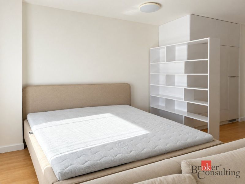 Schlafzimmer in einer Einzimmerwohnung mit Bett und weißen Regalen, Holzboden.